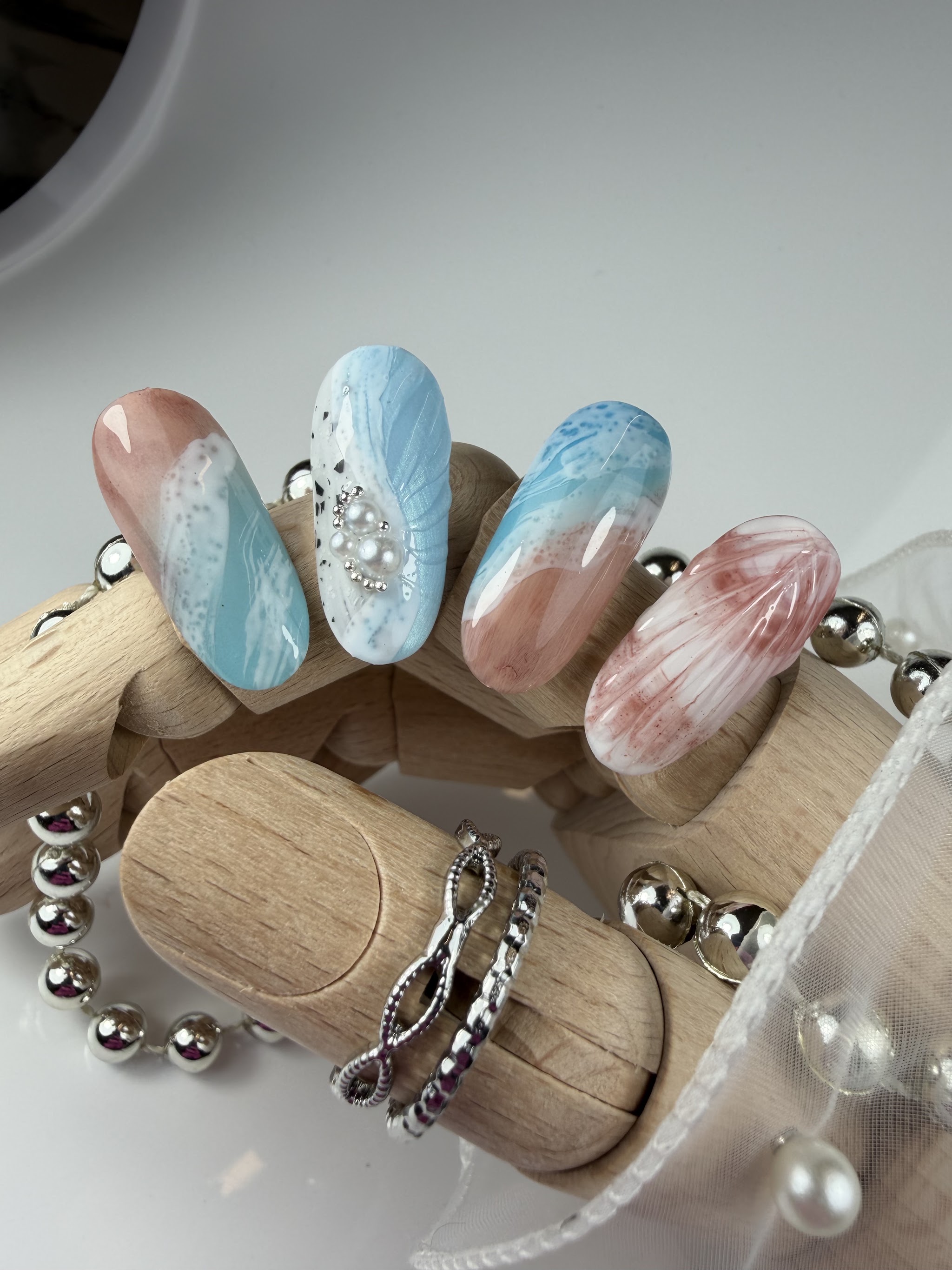 Nagels in zee- en schelptinten met parels, op een houten standaard in de studio